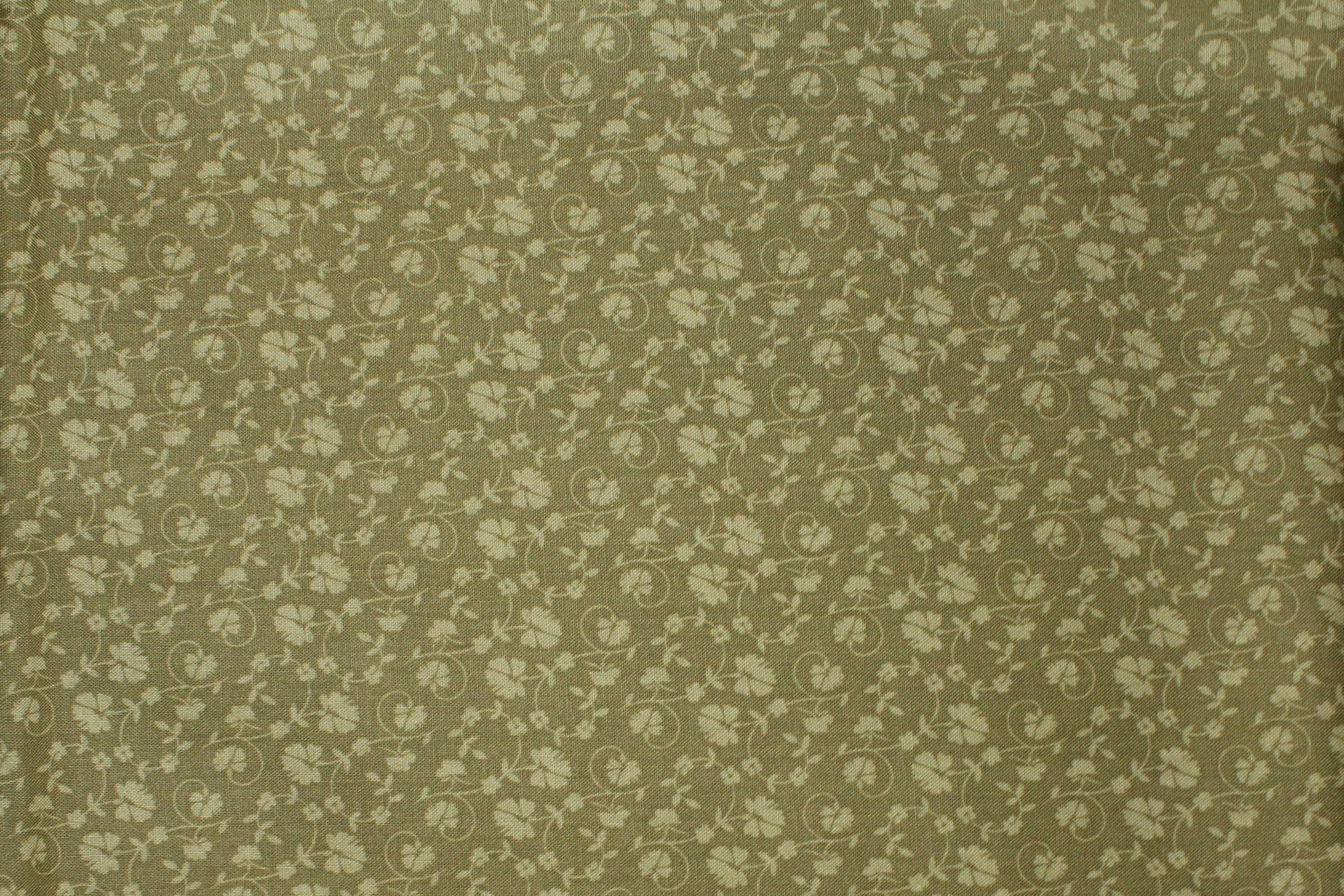 A close-up of a fabric surface with a small repeating floral or paisley-like pattern in muted olive green.