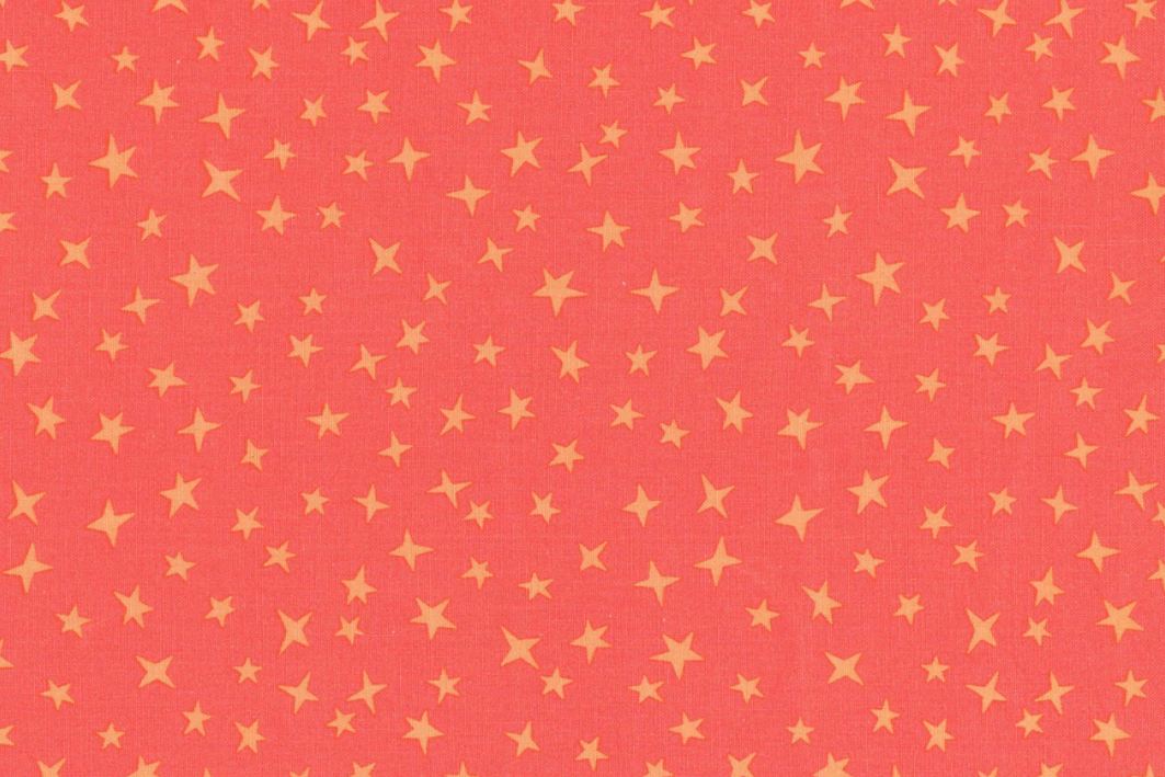 A close-up of a coral pink fabric with a repeating pattern of small yellow stars.