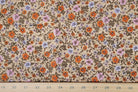 A close-up of a floral fabric pattern with small orange, purple, and pink flowers on a beige background, with a wooden ruler along the bottom edge showing measurements.