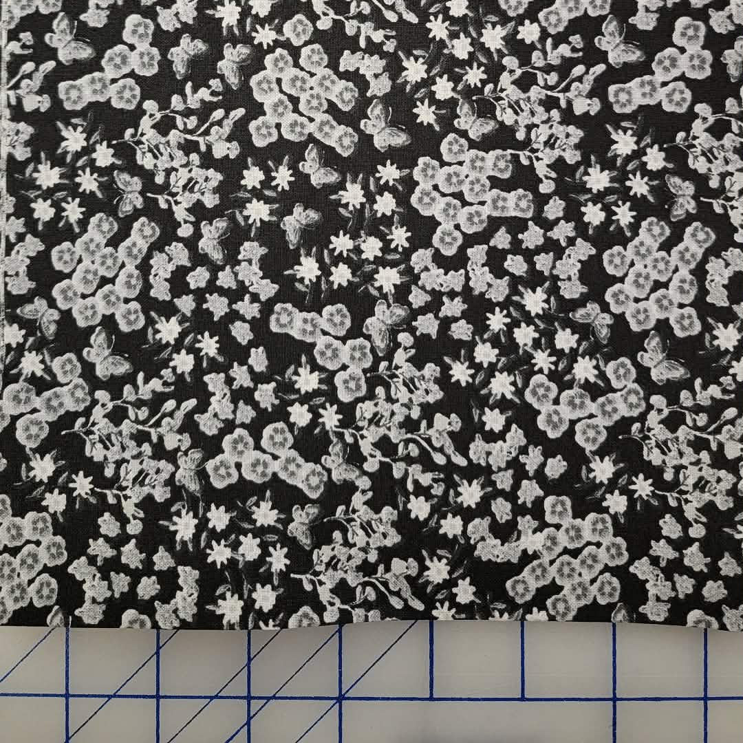 Black fabric with a dense white floral and lace-like pattern, laid flat on a blue-lined cutting mat.