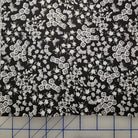 Black fabric with a dense white floral and lace-like pattern, laid flat on a blue-lined cutting mat.