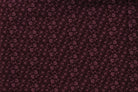 A close-up of a dark burgundy fabric with a repeating small floral or paisley-like print.