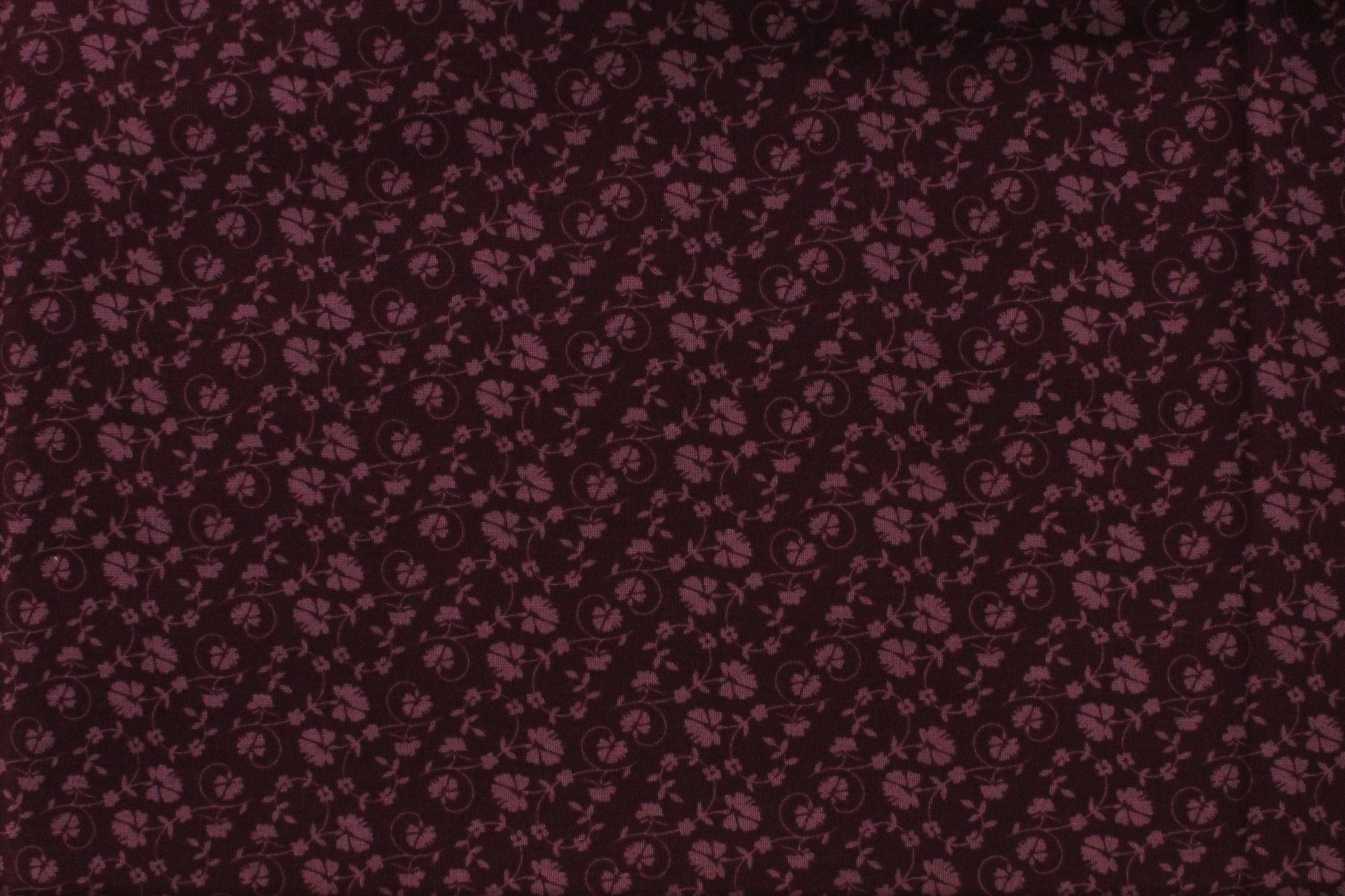 A close-up of a dark burgundy fabric with a repeating small floral or paisley-like print.