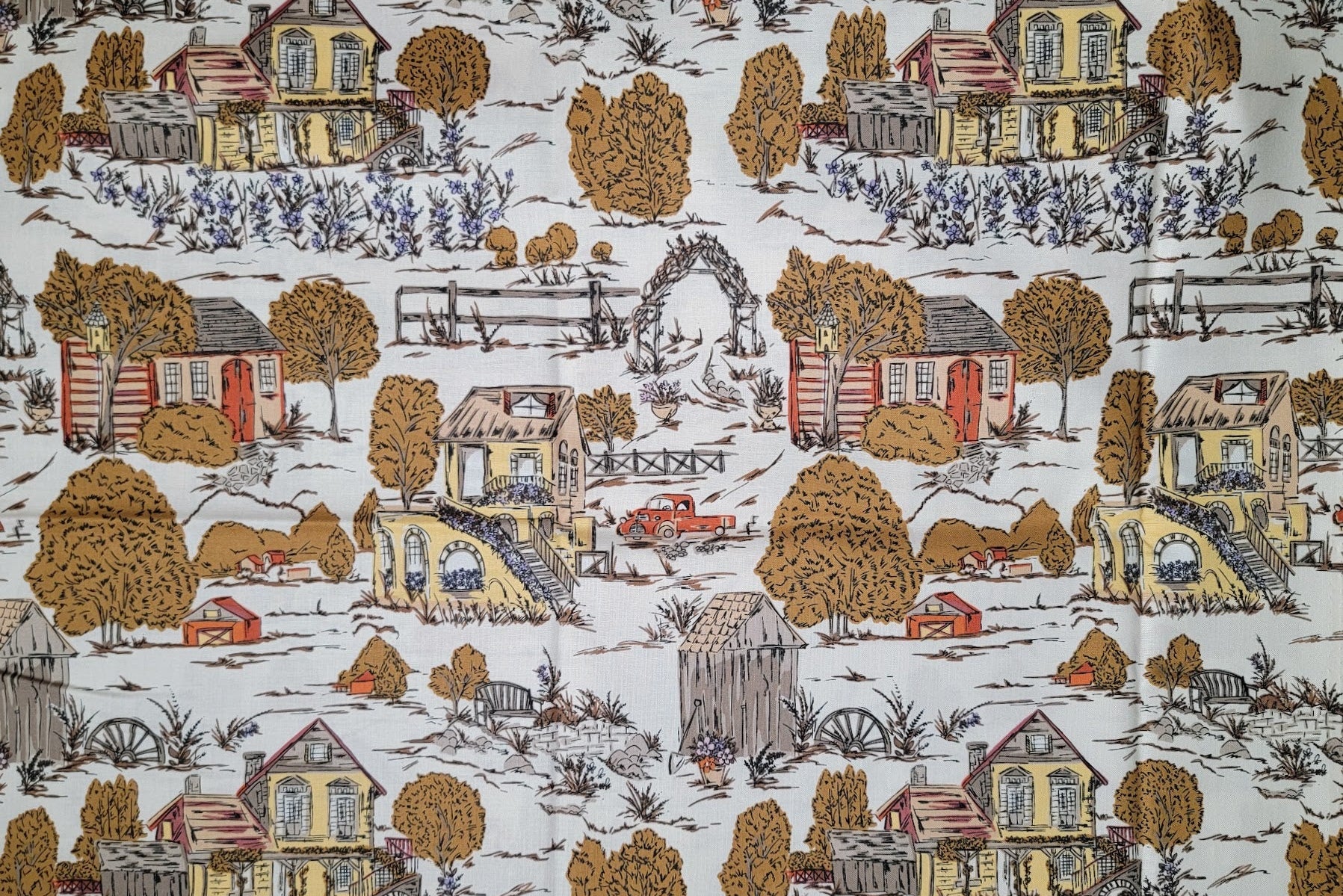 A close-up of a fabric pattern featuring a repeating western-style landscape print with yellow and red houses, brown trees, fences, and a red pickup truck on a white background.