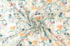 A close-up of a lightweight fabric with a delicate floral print, swirled in the center to show its soft texture and drape. The pattern features small yellow, orange, and teal flowers with green leaves on a warm off-white background.