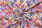 A close-up of a lightweight fabric swirled in the center to display its vibrant floral print. The pattern features purple, blue, yellow, and green flowers on a white background with bright red accents.