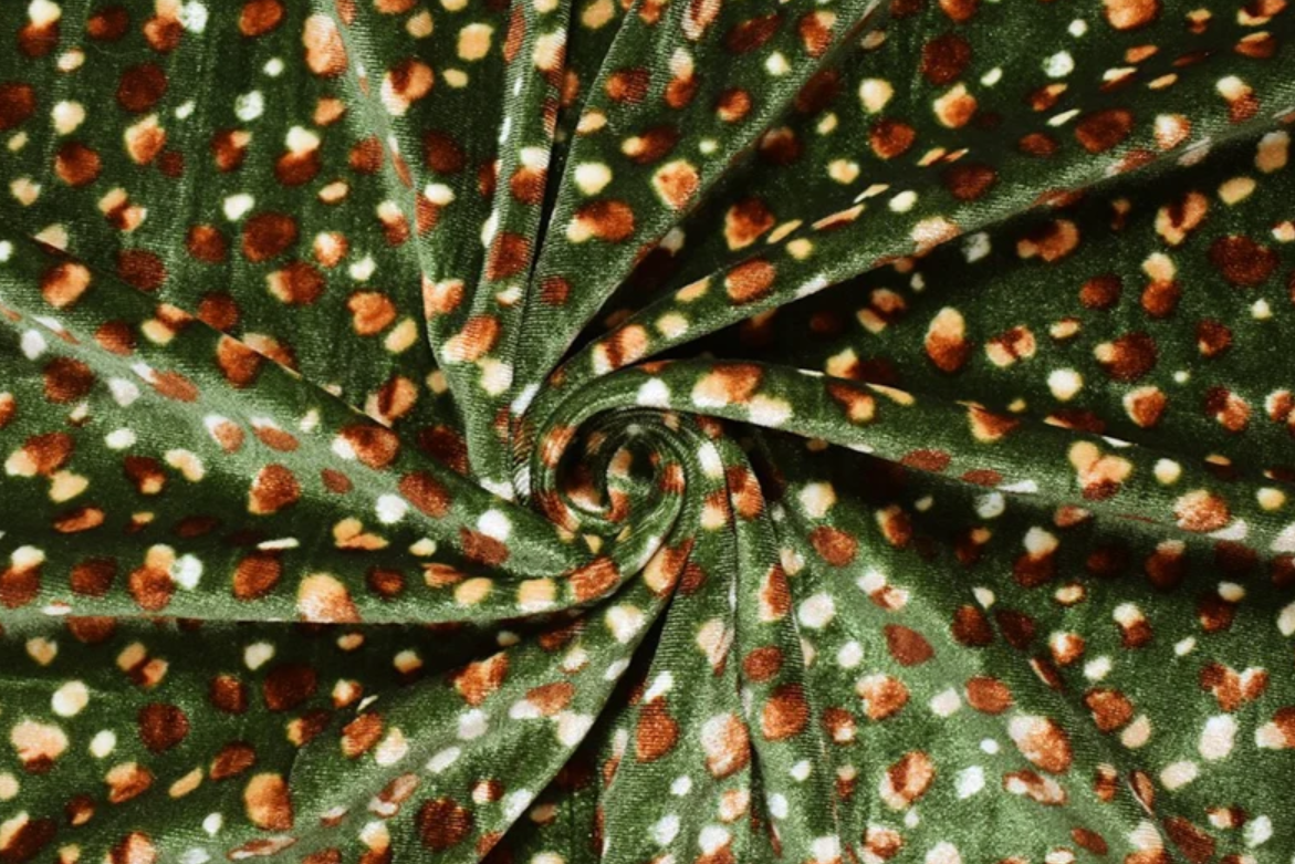 A close-up of dark green fabric arranged in a spiral, featuring an all-over pattern of small brown spots and scattered white dots.