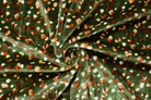 A close-up of dark green fabric arranged in a spiral, featuring an all-over pattern of small brown spots and scattered white dots.
