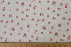 White fabric with a repeating pattern of red and brown mushrooms and small red dots, shown with a wooden ruler along the bottom edge for scale.