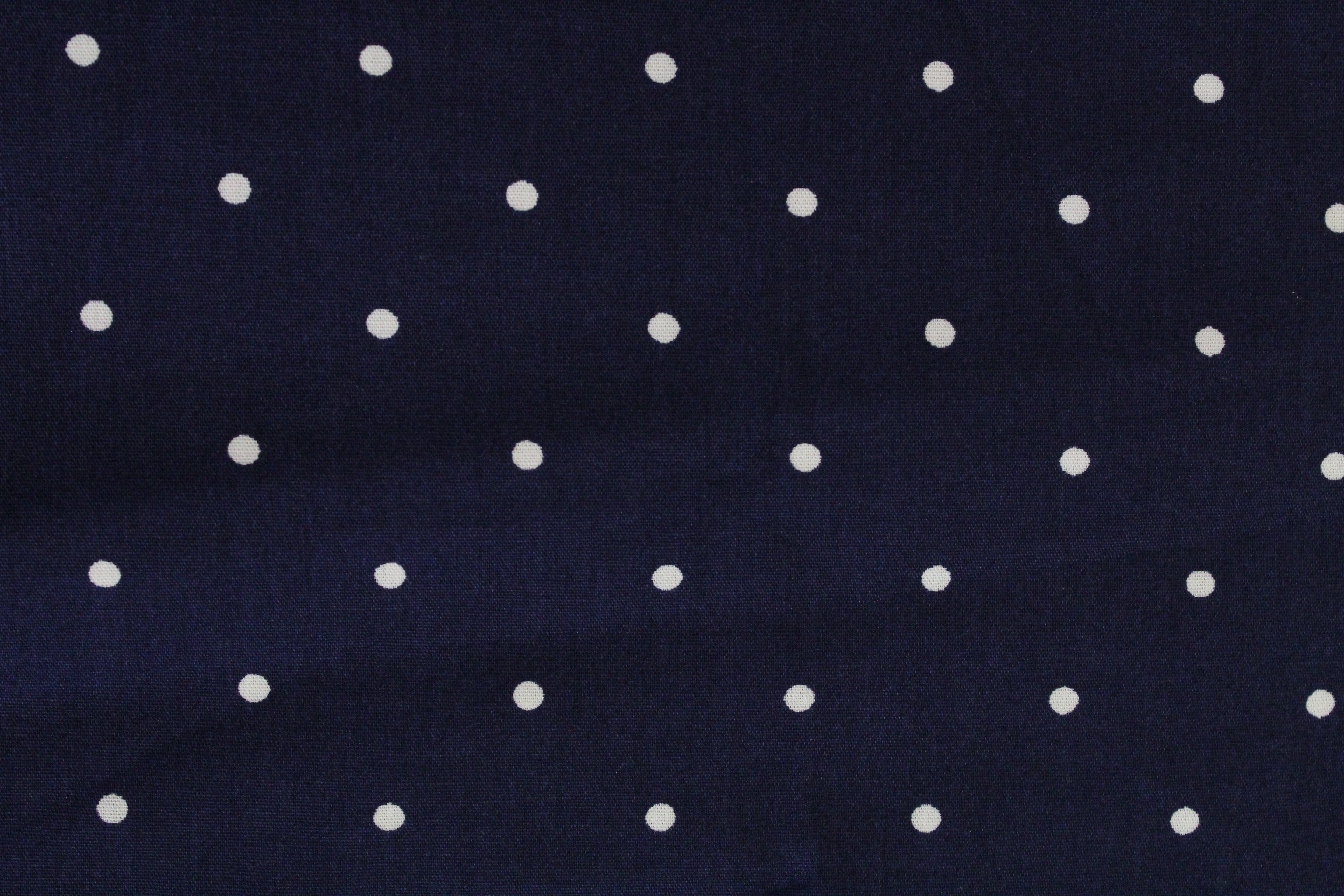 A close-up of a navy blue fabric with a repeating pattern of small white polka dots.
