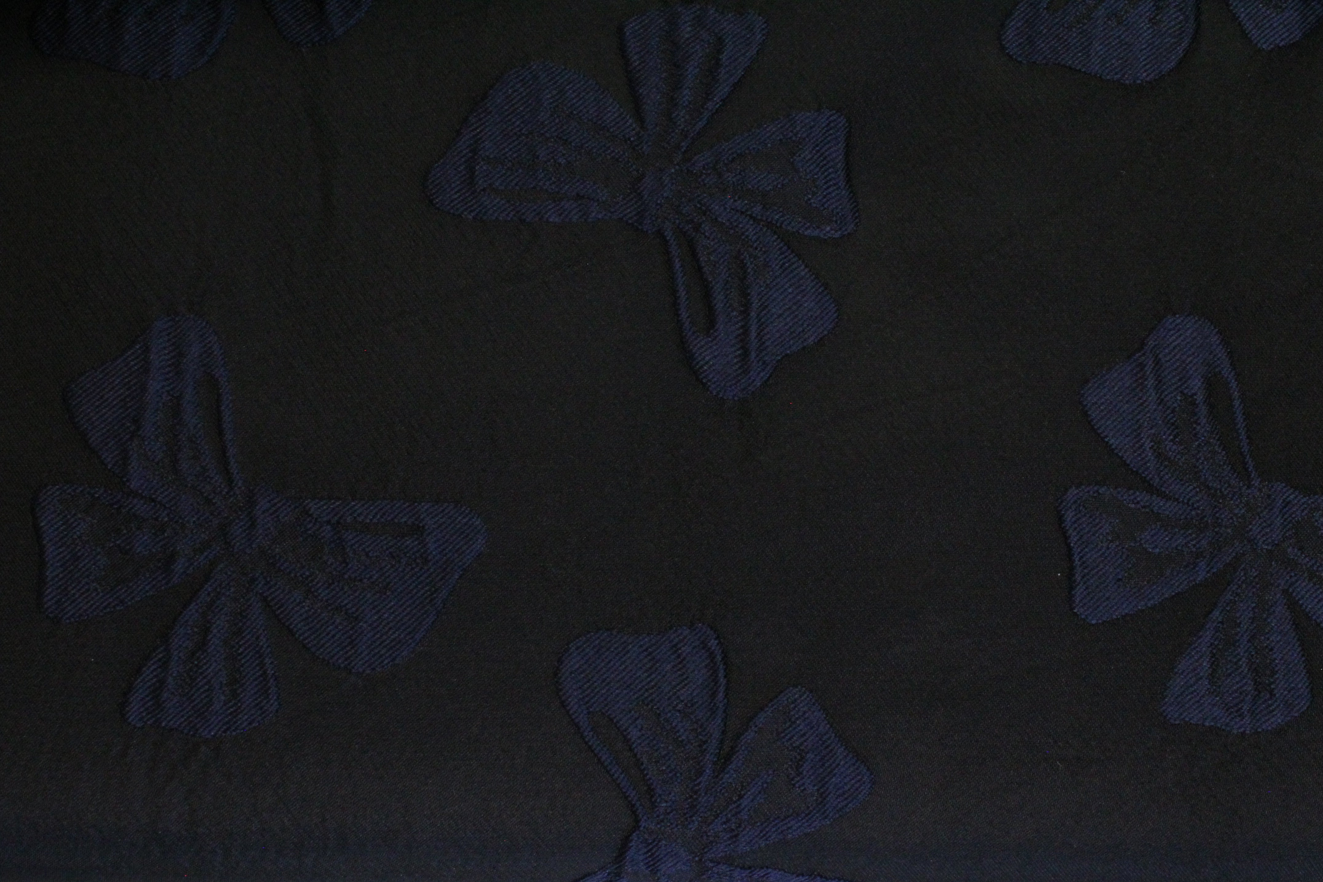 A close-up of a dark fabric with a repeating bow pattern.