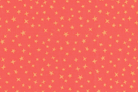 A close-up of a coral pink fabric with a repeating pattern of small yellow stars.