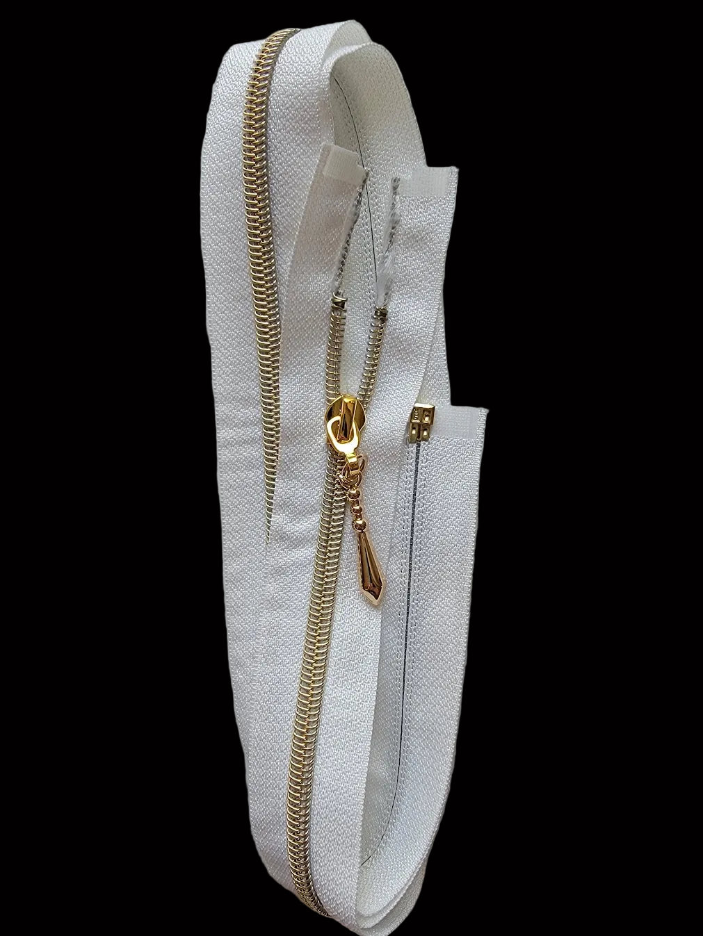 A white textured zipper tape strip with a gold-toned metal zipper and pull tab, photographed against a plain light gray background.